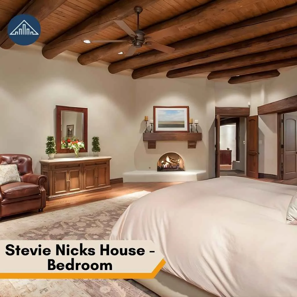 A cozy fireplace and rustic wooden ceiling beams enhance the warm bedroom within Stevie Nicks House.